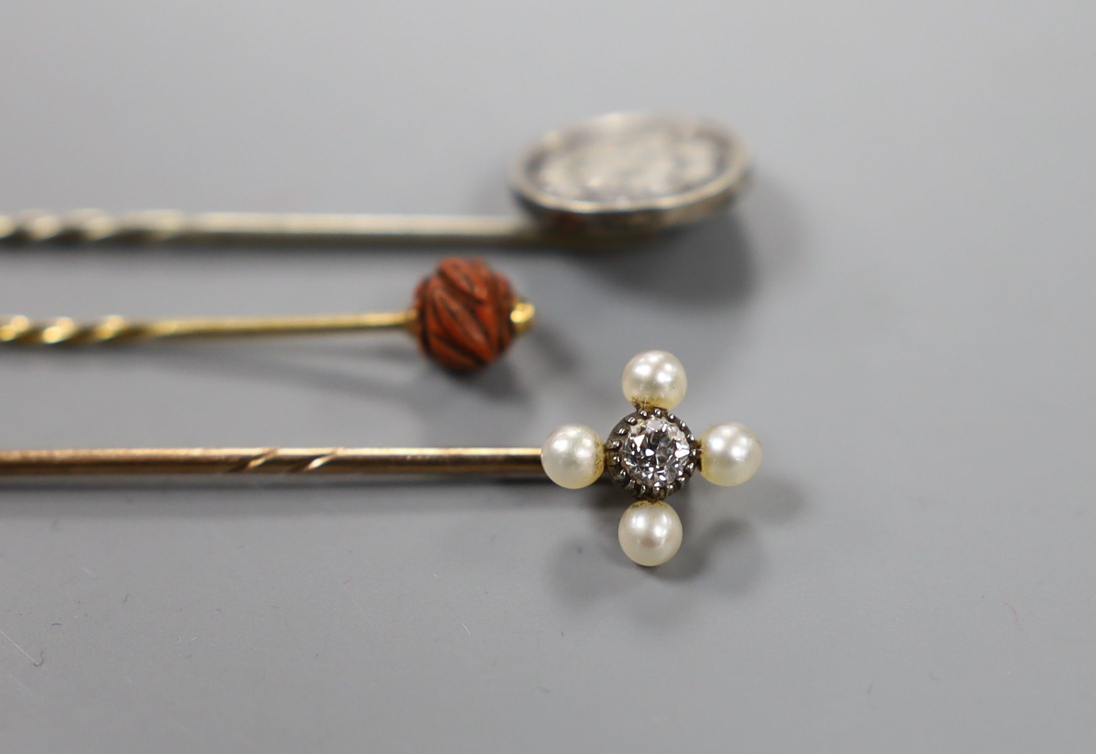 An Edwardian yellow metal, seed pearl and diamond set stick pin, 57mm and two other stick pins.